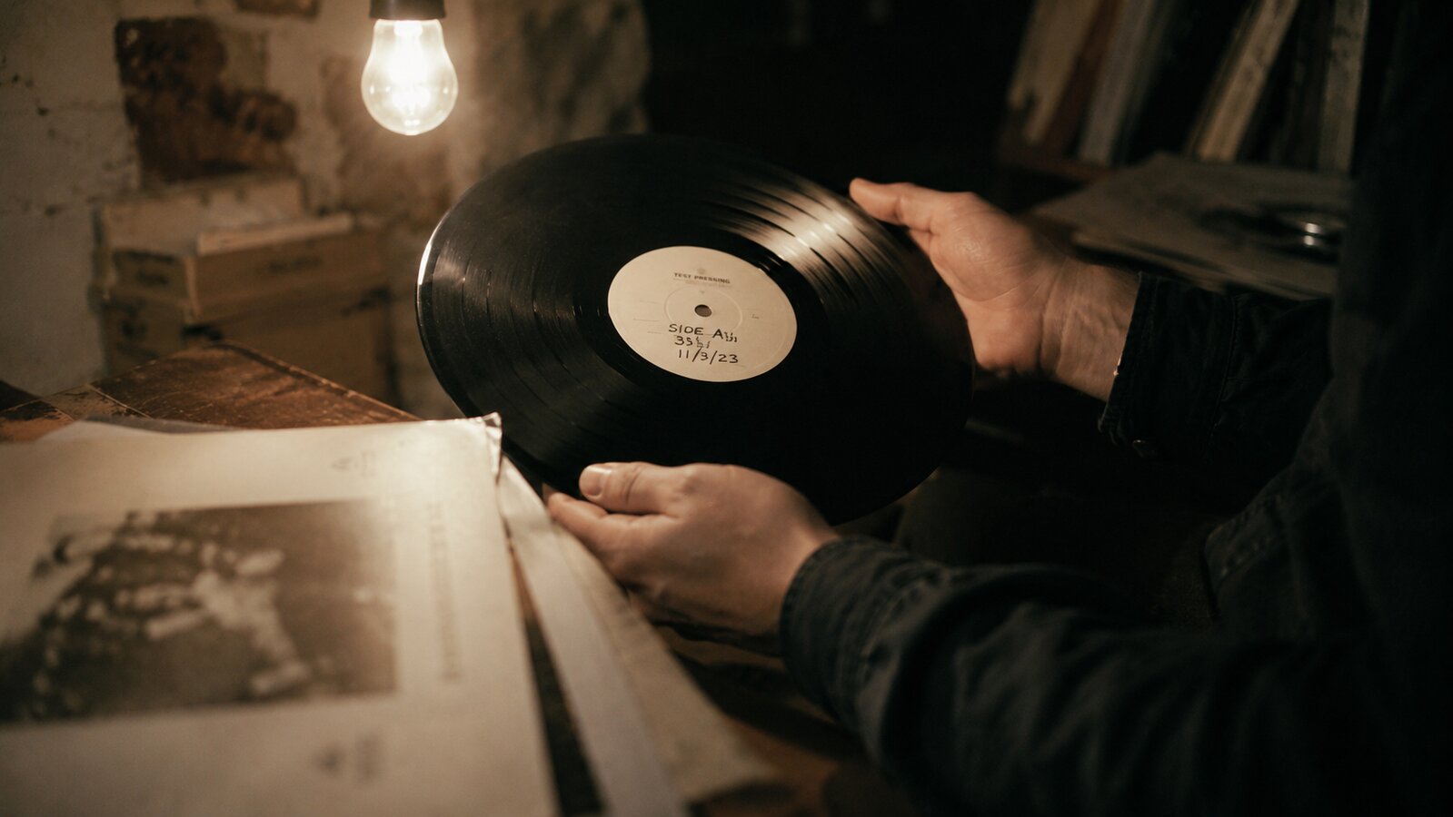 Hands holding a vinyl test pressing under a single warm bulb