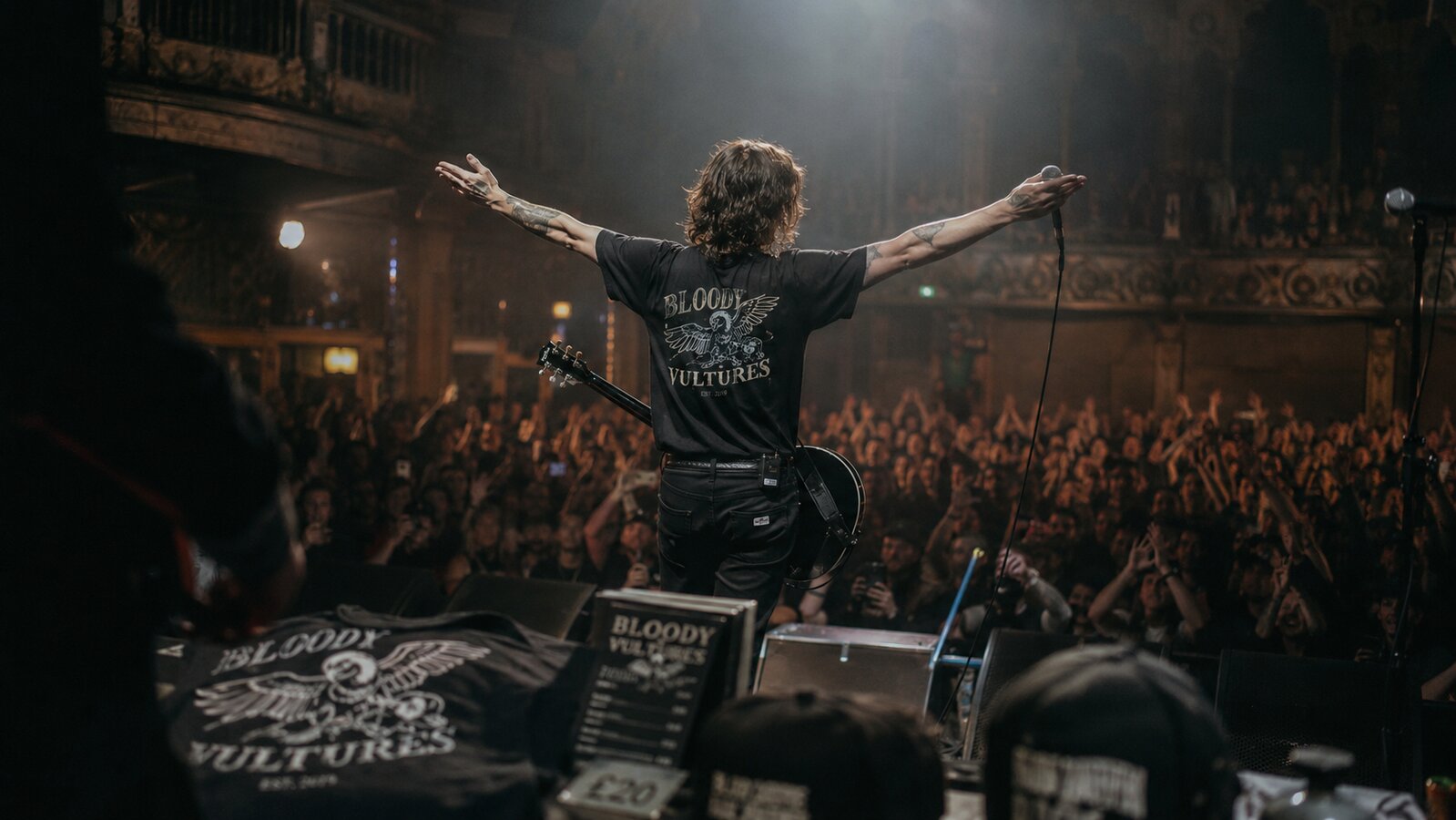 Musician on stage wearing their own band tee with the crowd silhouetted