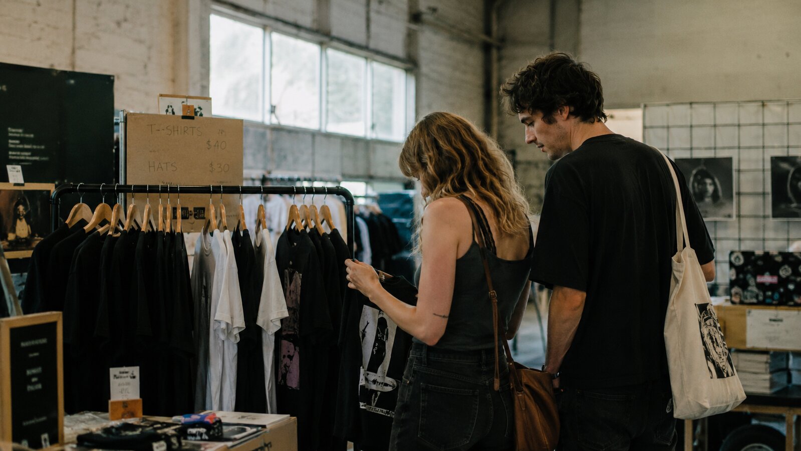 Pop-up artist merch shop in a daylit warehouse with browsing fans