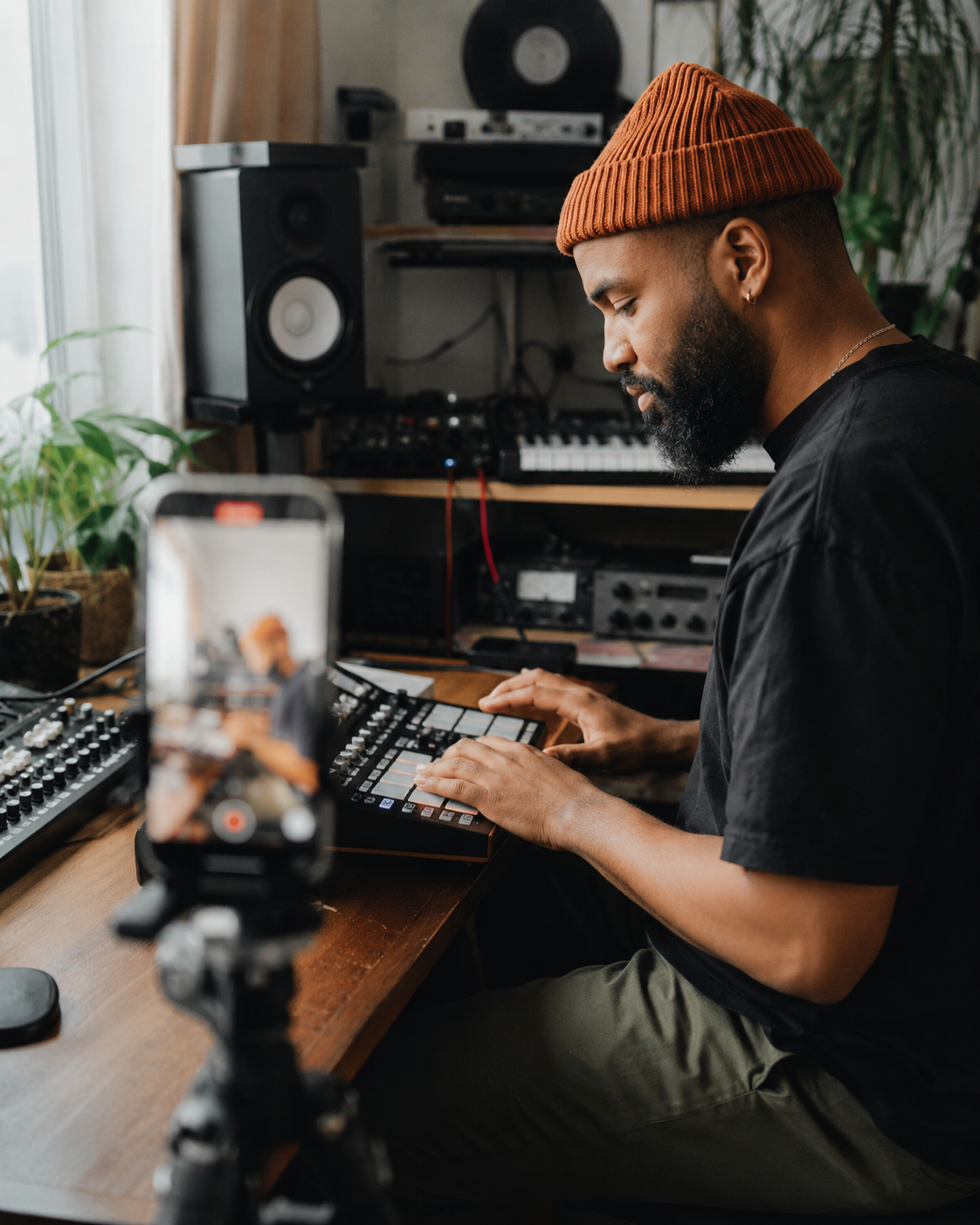 Music producer filming beatmaking content on a smartphone while working at a studio desk.