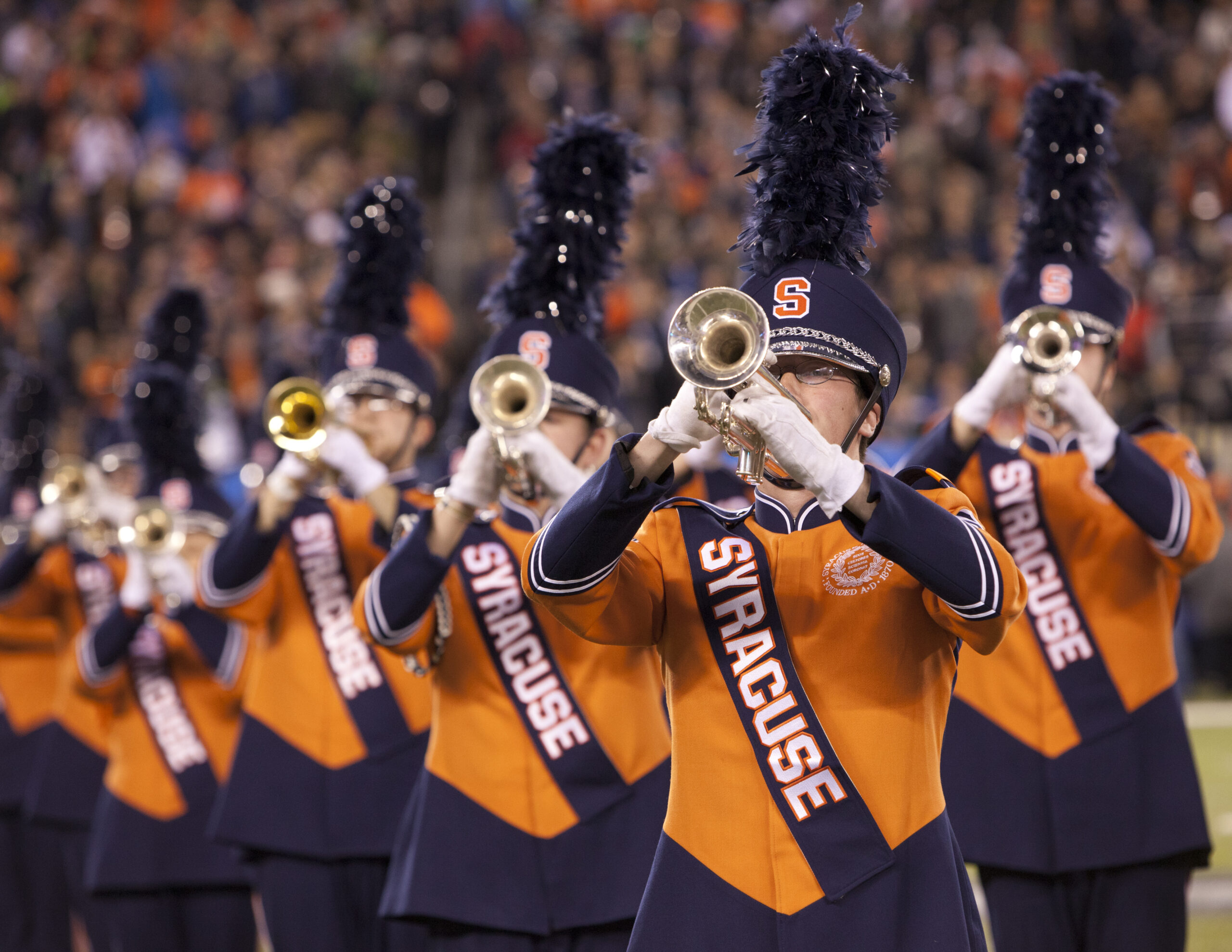 Syracuse University Marching Band in orange uniforms performing on the field at Super Bowl XLVIII in February 2014, brass section visible in the foreground